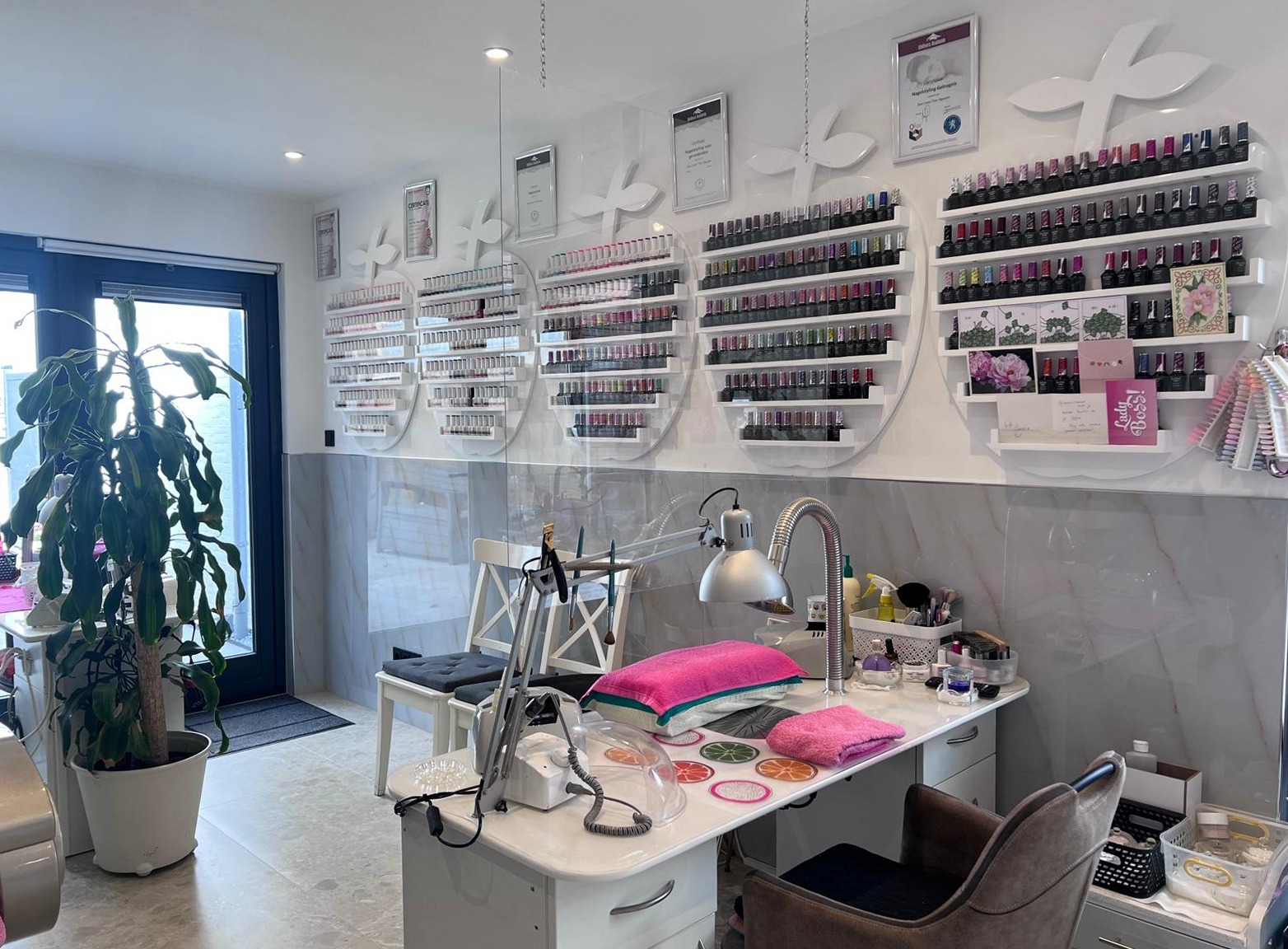 De manicuretafel in de studio, met de wand vol gellak op ronde witte planken